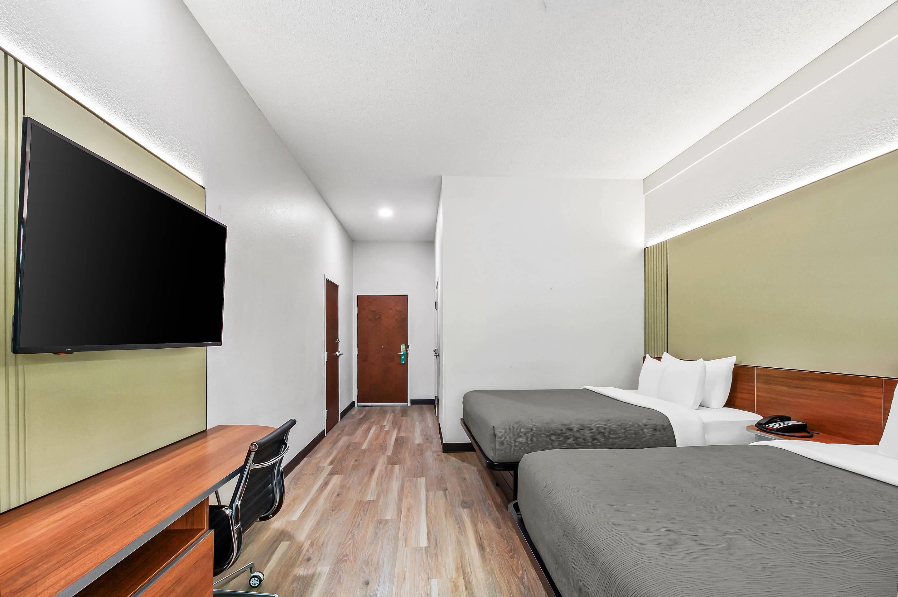 Ein Hotelzimmer mit Flachbildfernseher, Schreibtisch, zwei Betten und Holzboden.