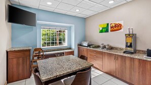 A kitchen with granite countertops, wooden cabinets, a flat-screen TV, a window with a view of greenery, and a waffle machine.