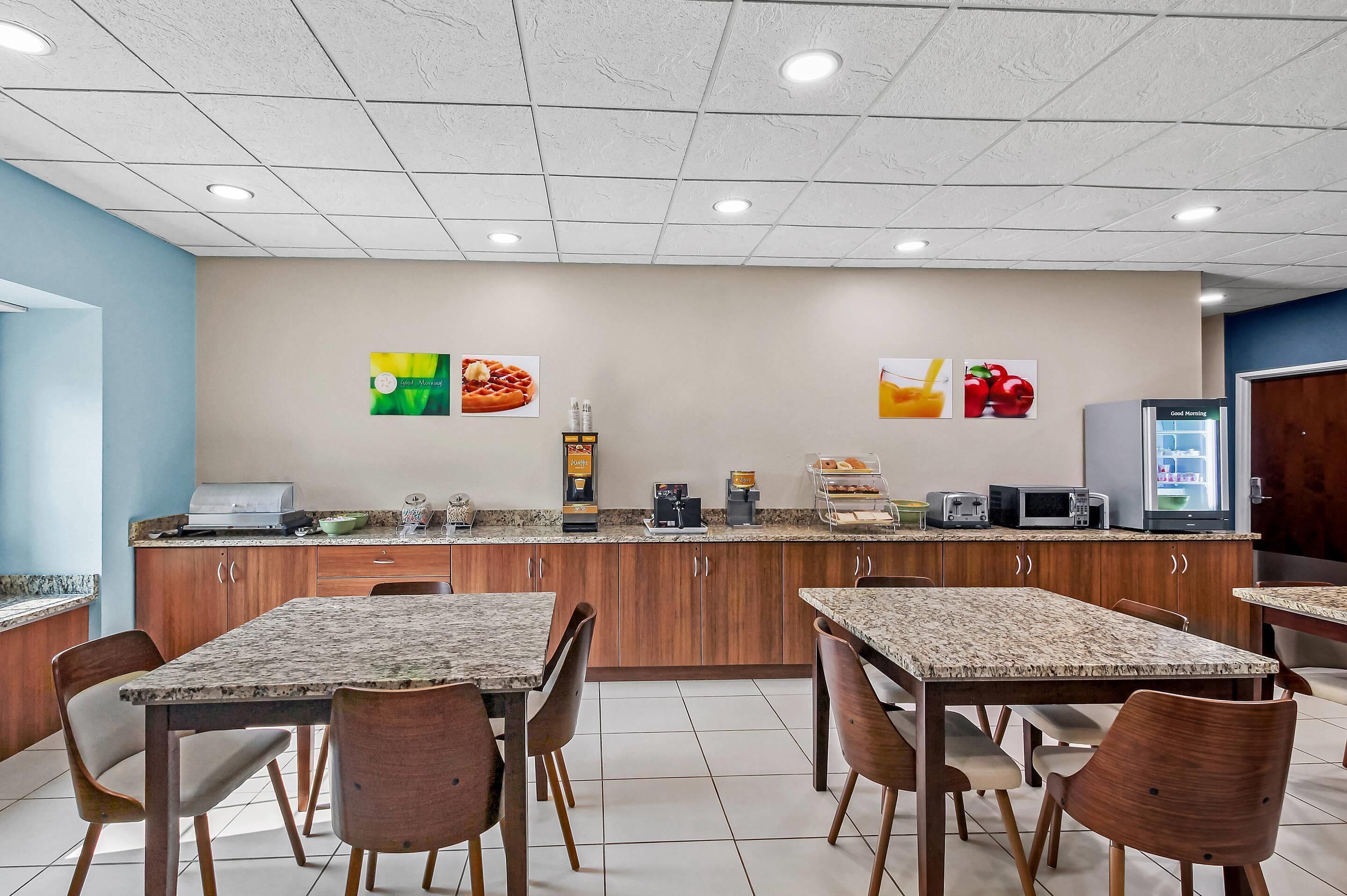 A dining area with granite-topped tables and wooden chairs, a kitchen counter with appliances, and a refrigerator.