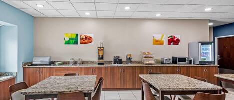 A dining area with granite-topped tables and wooden chairs, a kitchen counter with appliances, and a refrigerator.