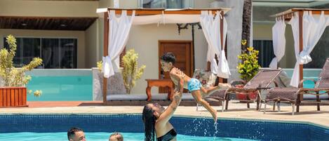 A swimming pool with lounge chairs and a covered area.