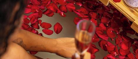 A bathtub filled with rose petals and a wooden tray with a candle.