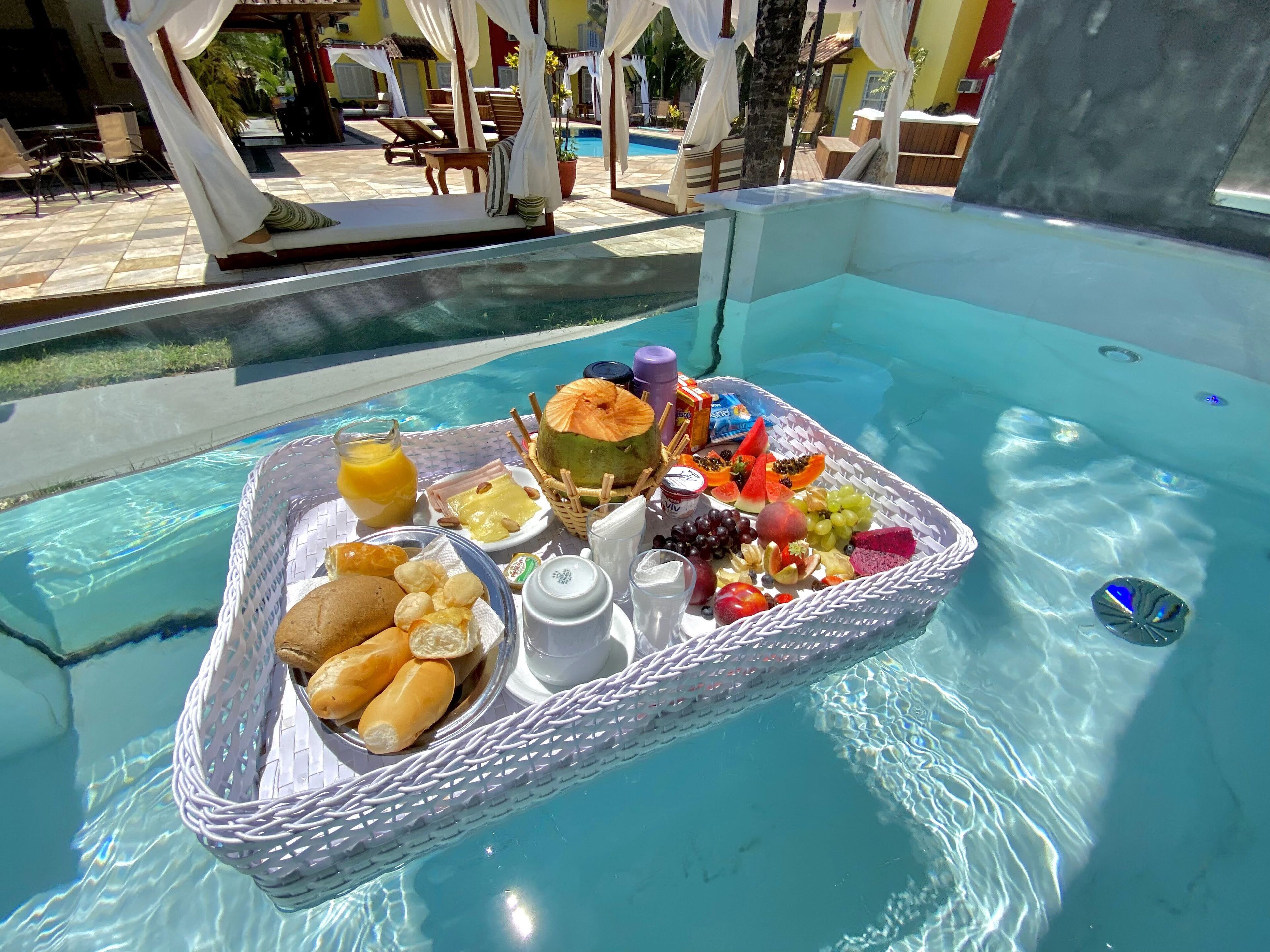 A poolside breakfast tray with fruits, bread, and beverages.