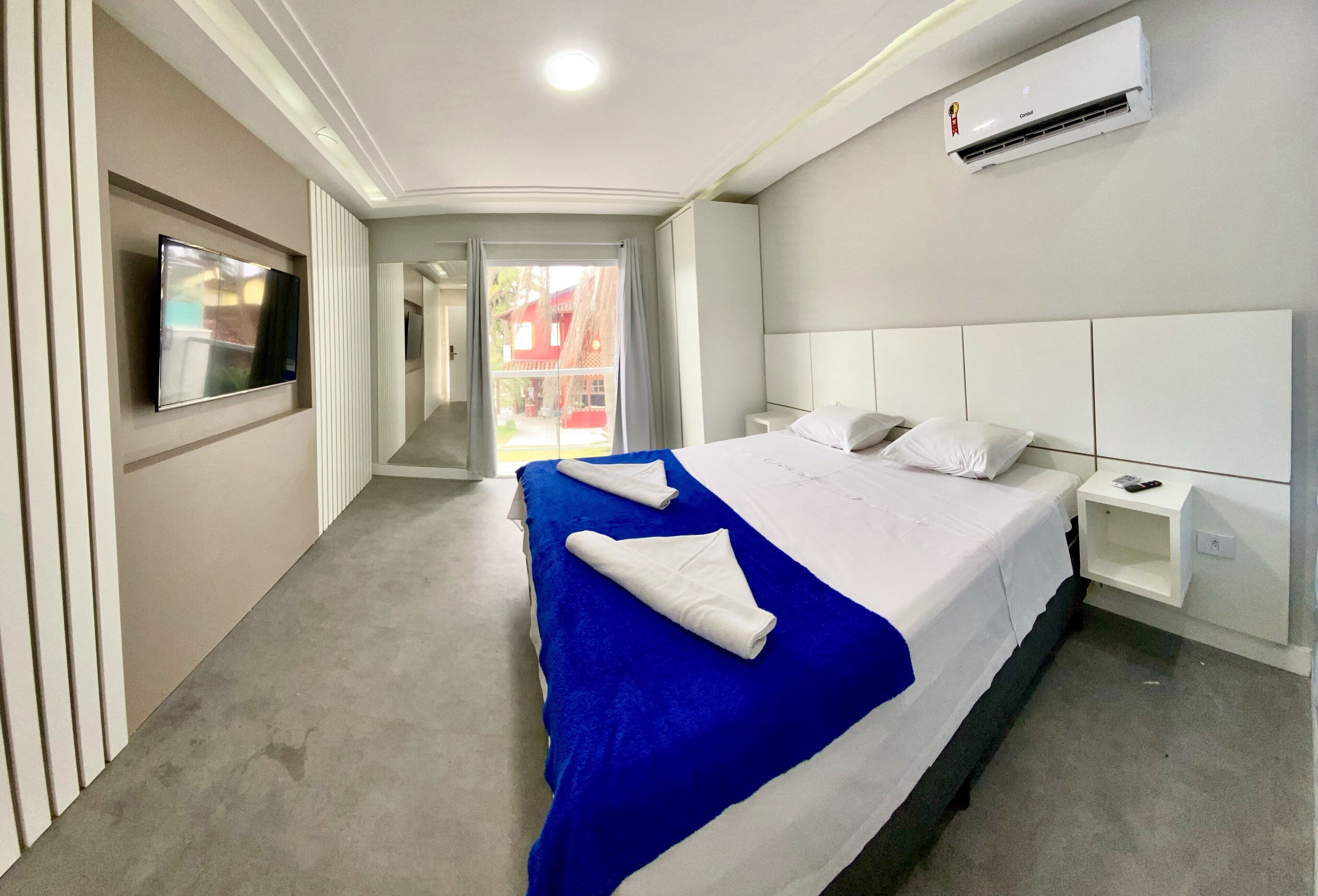 A hotel room with a large bed, a flat-screen TV mounted on the wall, and an air conditioning unit.