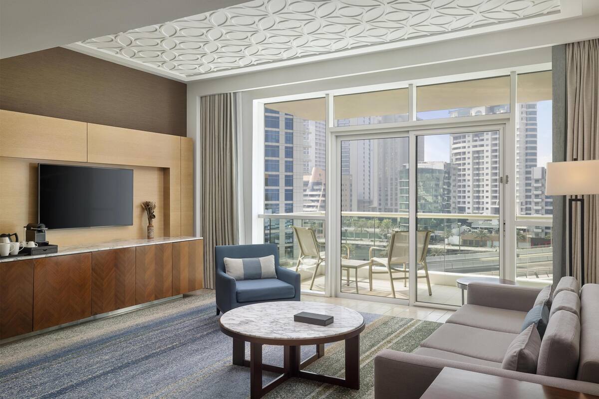 Une chambre d’hôtel moderne dotée d’un grand balcon, d’un téléviseur à écran plat, d’un canapé, d’une table basse et d’un plafond décoratif.