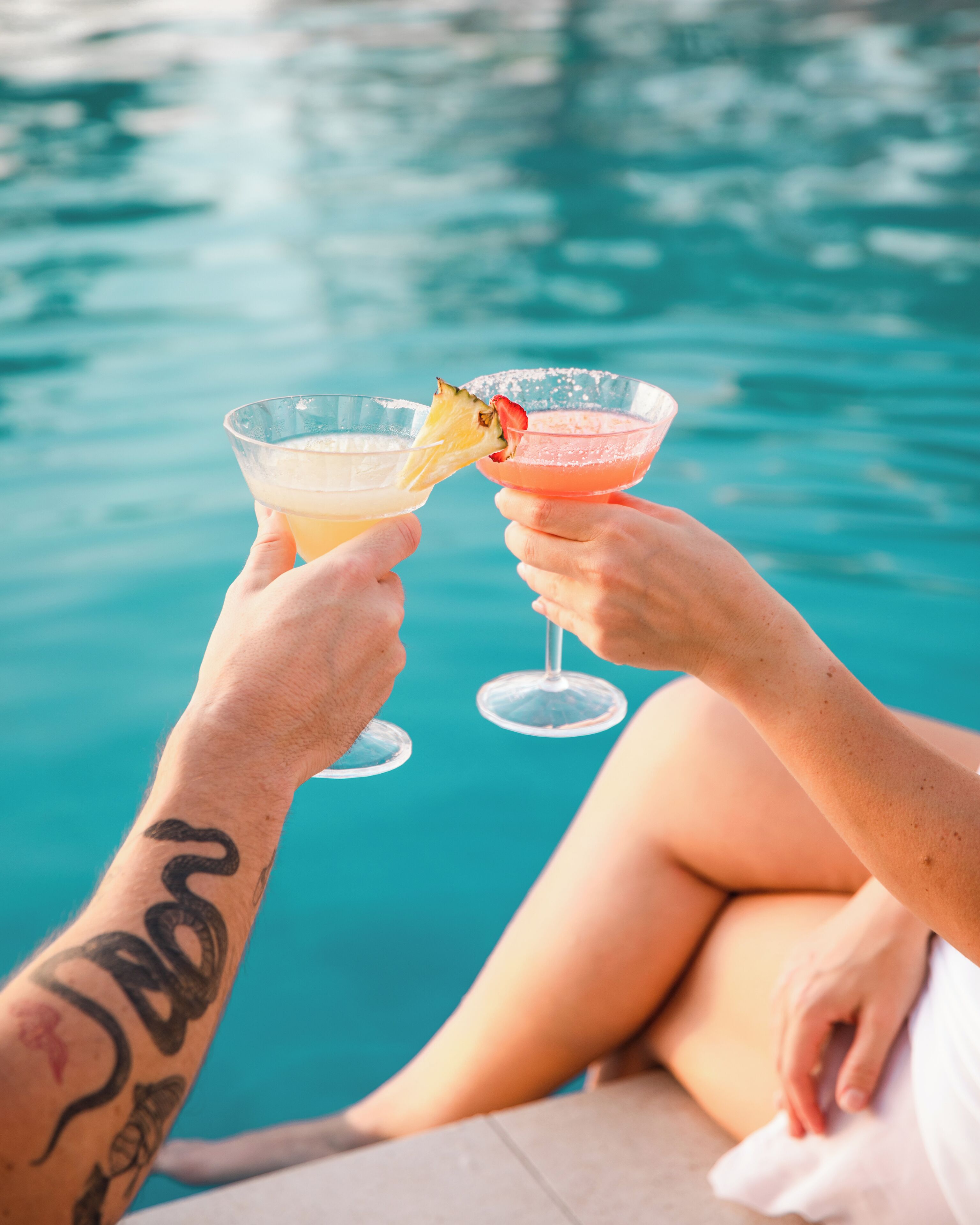 Dos personas brindando con bebidas junto a una piscina.