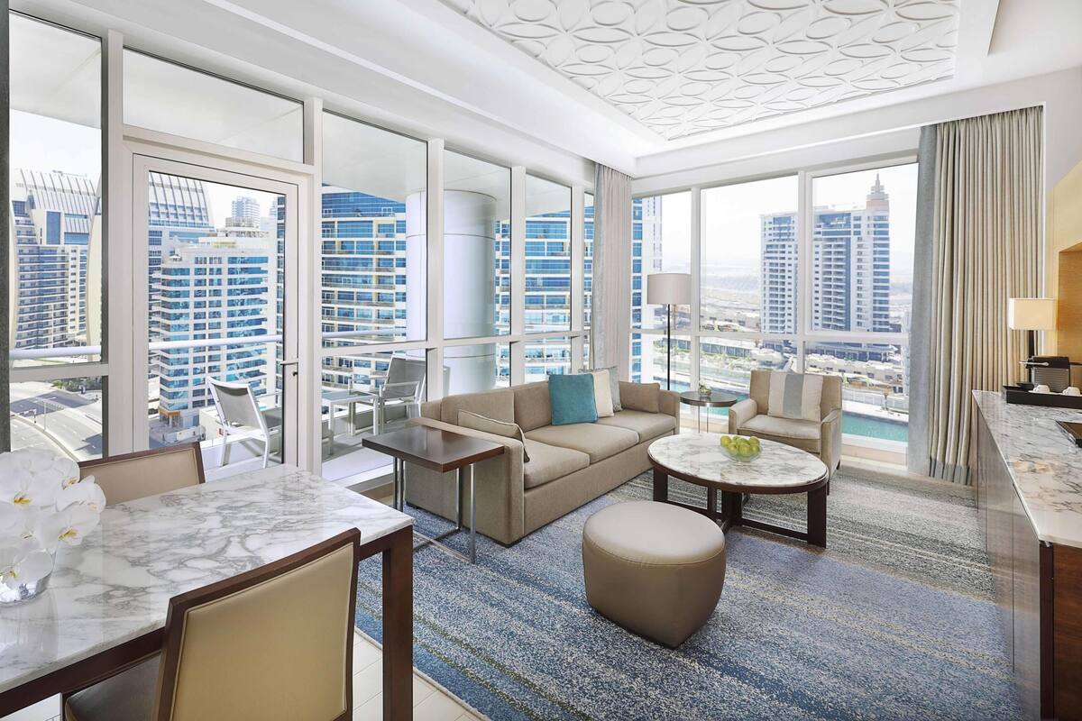 Une chambre d’hôtel moderne avec vue sur la ville, une table à manger en marbre, un canapé, une table basse et un petit balcon.