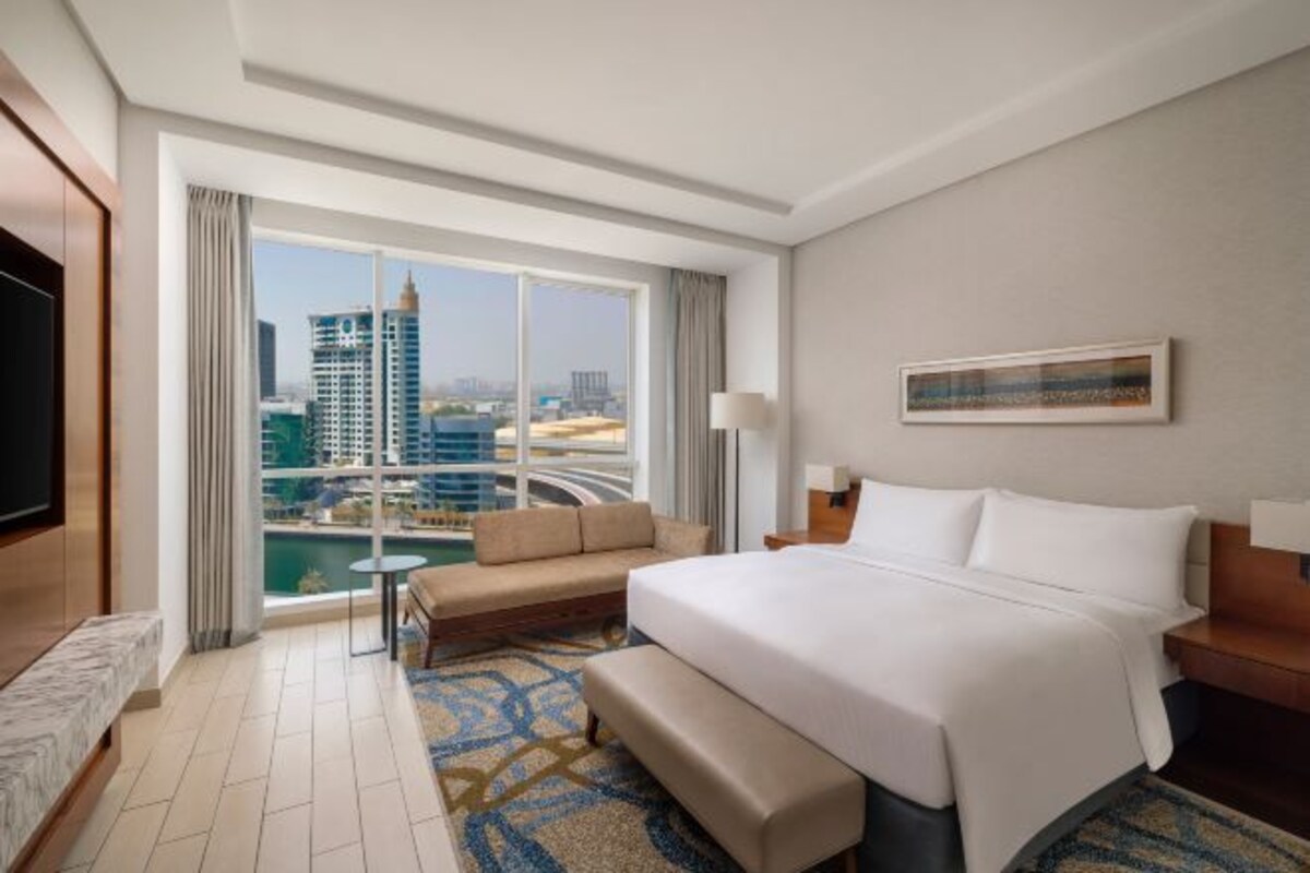 Une chambre d’hôtel avec un grand lit, un canapé, une télévision et une vue sur le paysage urbain.