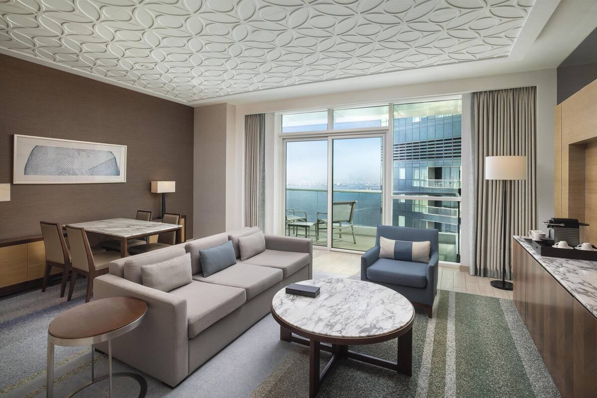 Une chambre d’hôtel moderne équipée d’un canapé, d’un fauteuil, d’une table à manger et d’un balcon offrant une vue sur la ville.