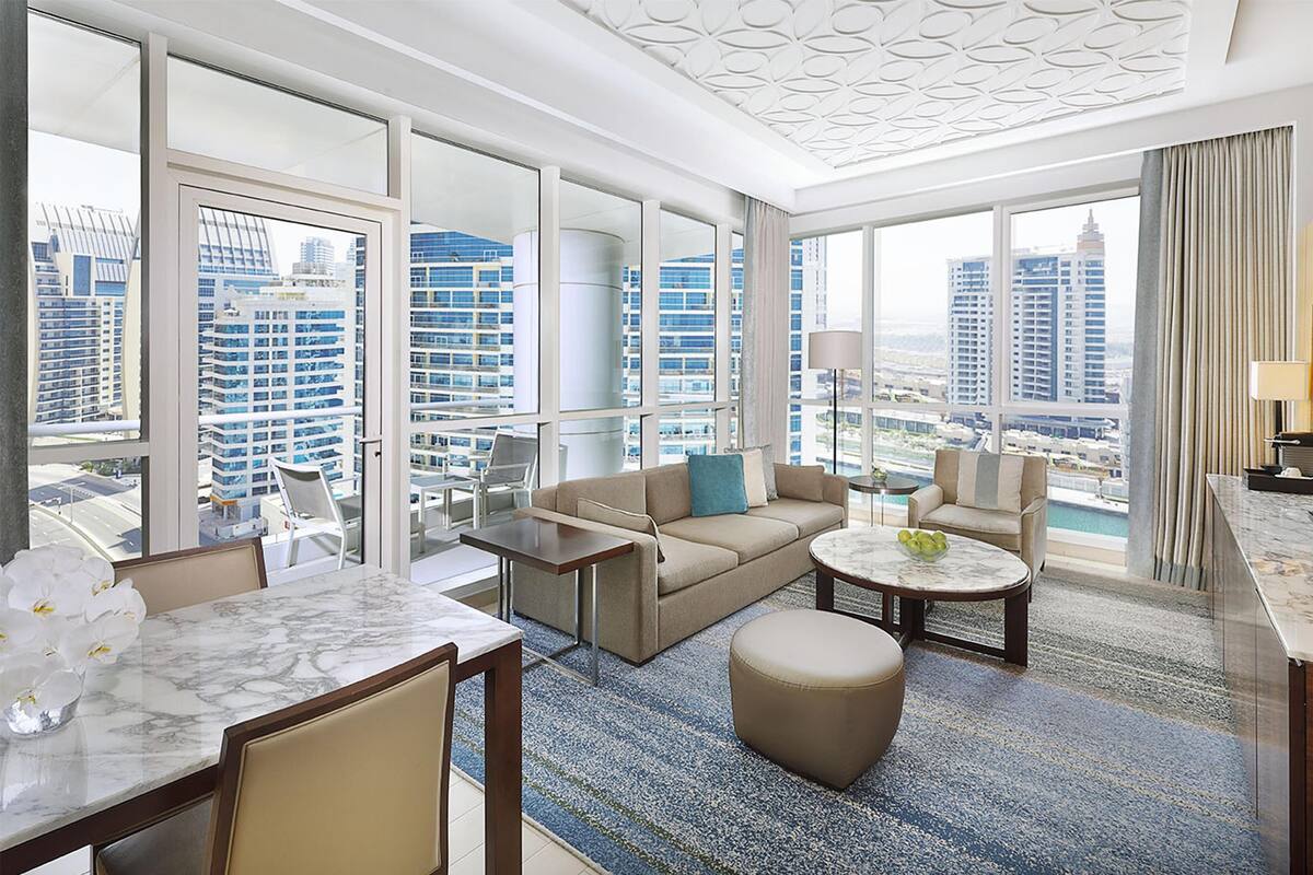 Une chambre d’hôtel spacieuse avec un grand balcon, un canapé, une table basse et un coin repas doté d’une table en marbre.