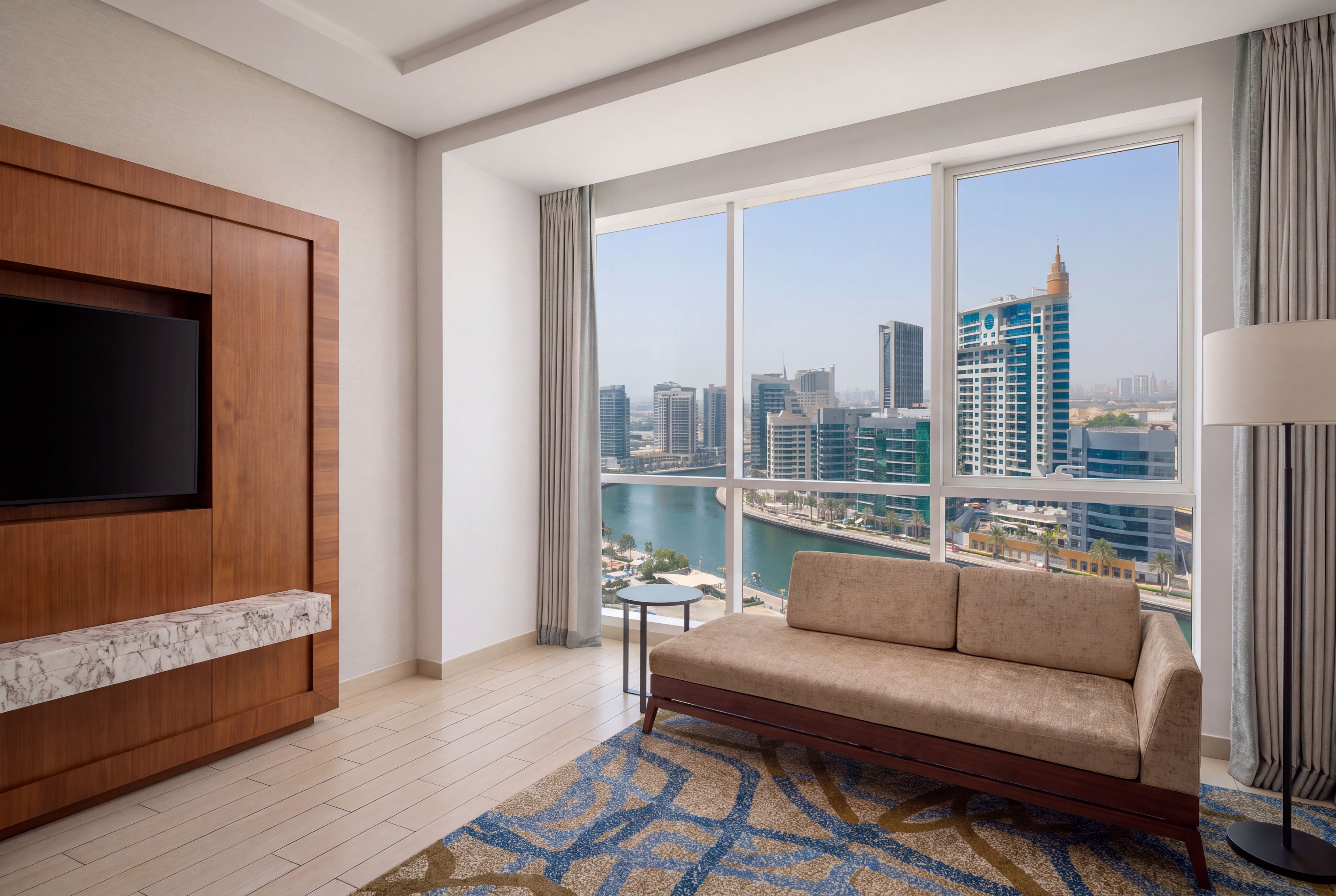 A modern living room with a large TV, a sofa, and a view of a cityscape and water.