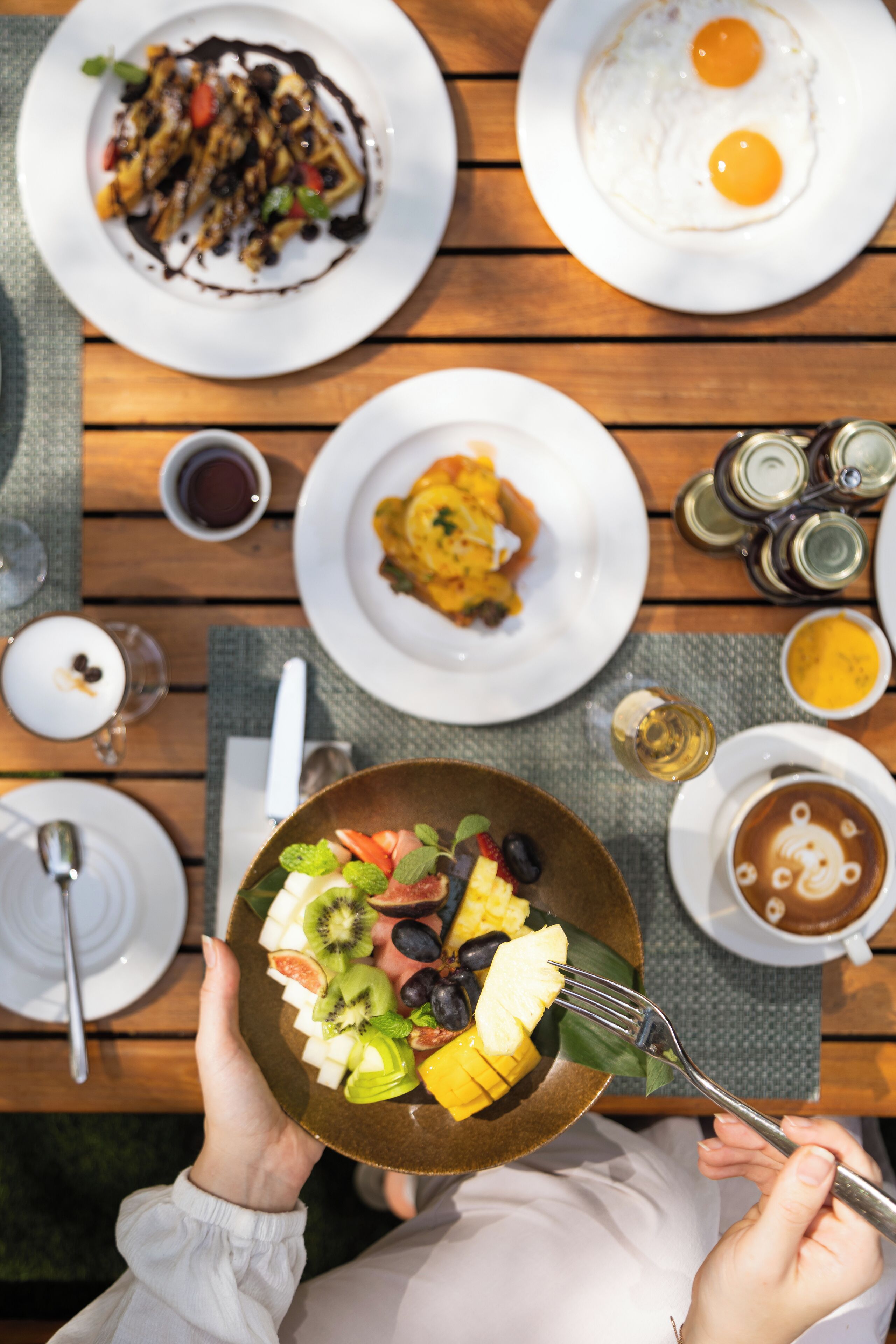 A dining table with various dishes, including a plate of fruit salad, a plate of eggs, and a plate of pancakes.