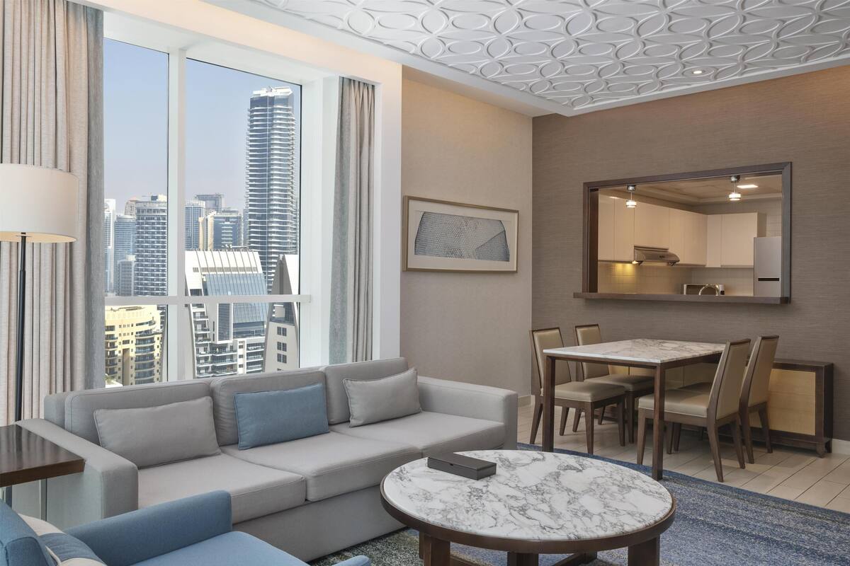 Une chambre d’hôtel moderne dotée d’une grande fenêtre, d’un canapé, d’une table à manger et d’un coin cuisine.