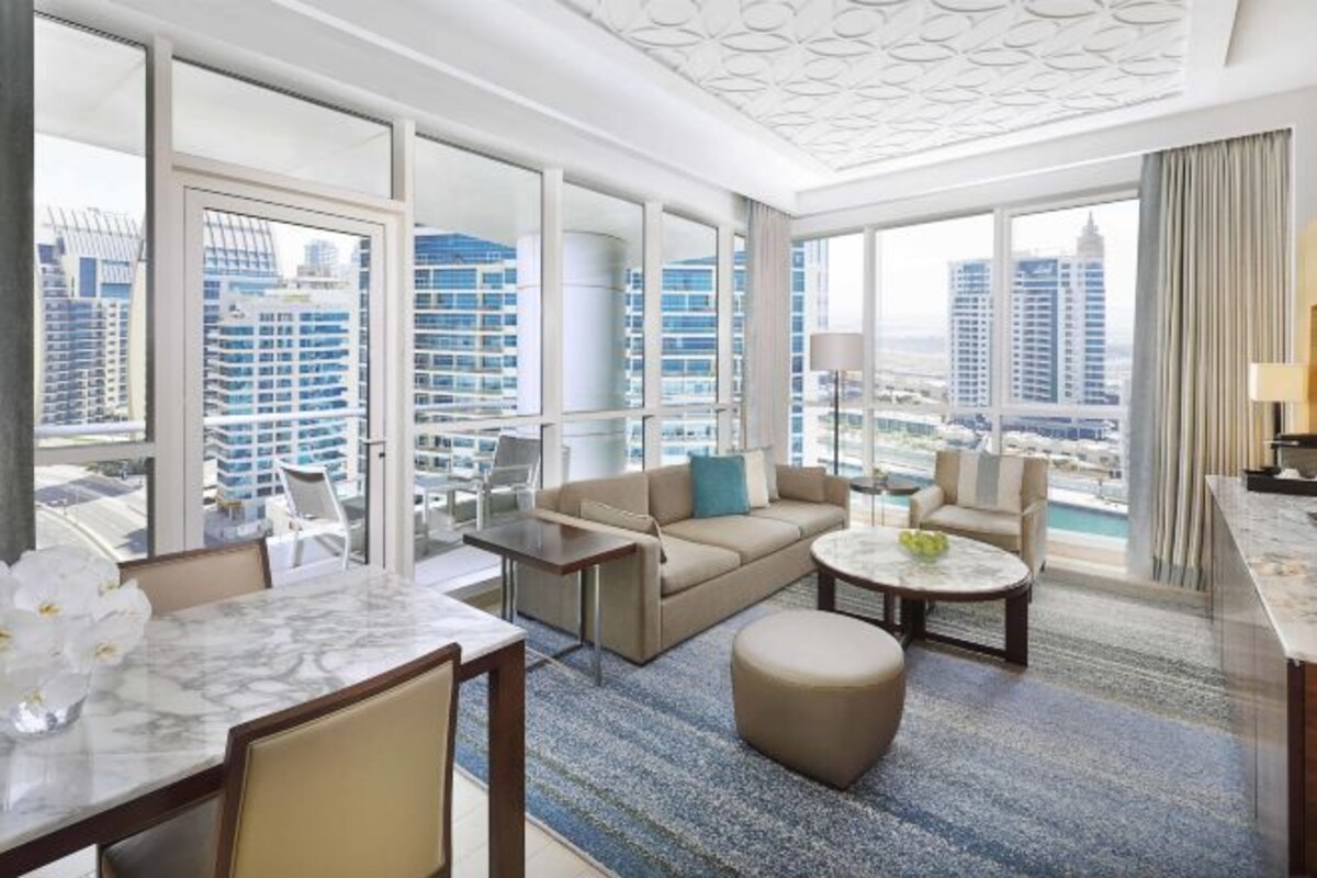 Une chambre d’hôtel moderne dotée d’une grande fenêtre, d’un canapé, d’une table basse et d’un coin repas.