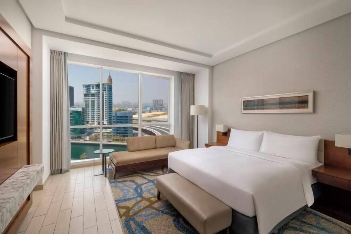 Een hotelkamer met een groot raam, een bed, een bank, een televisie en een kleine tafel.