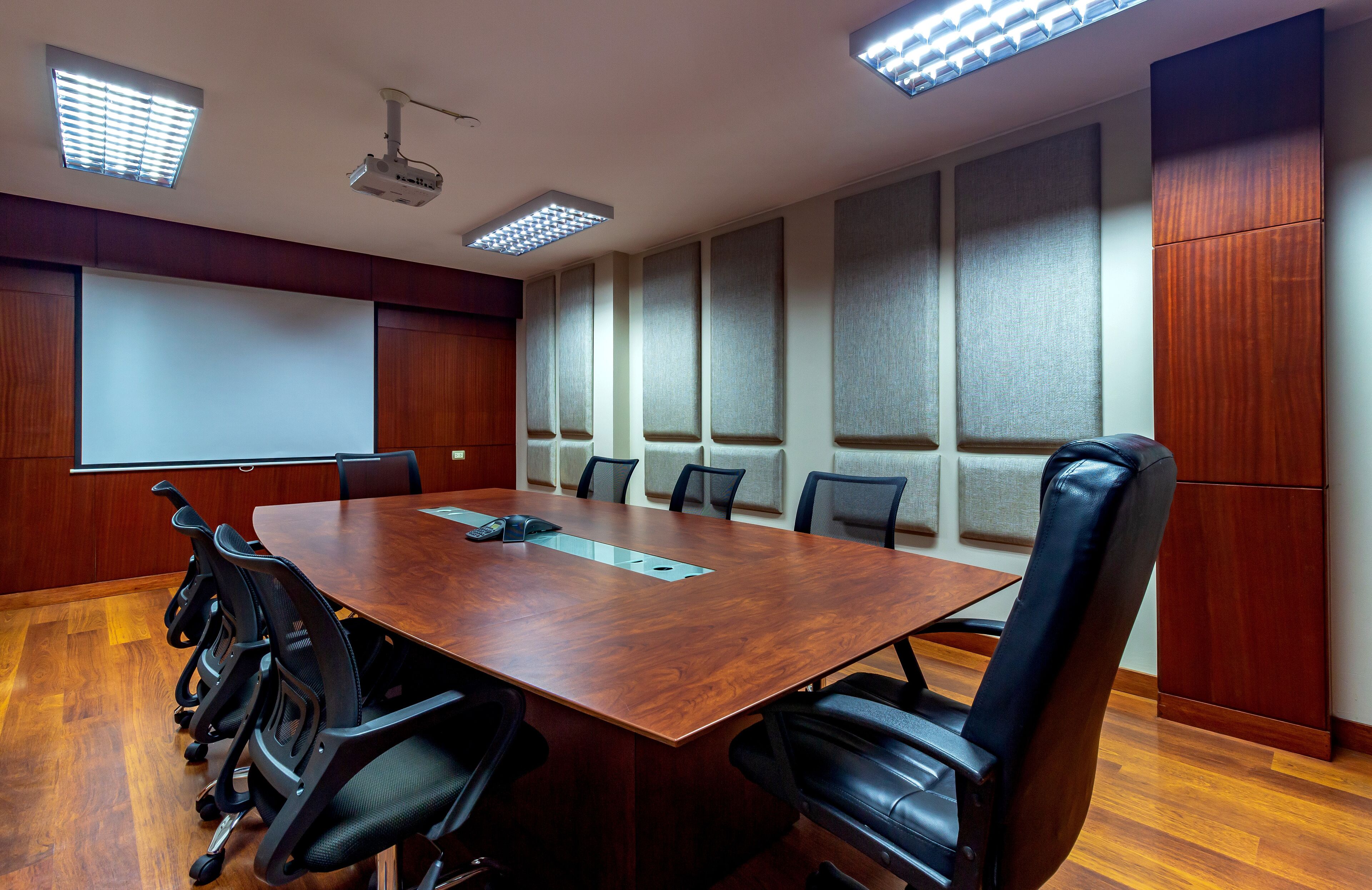 A conference room with a large wooden table, black chairs, a projector, and a white screen.