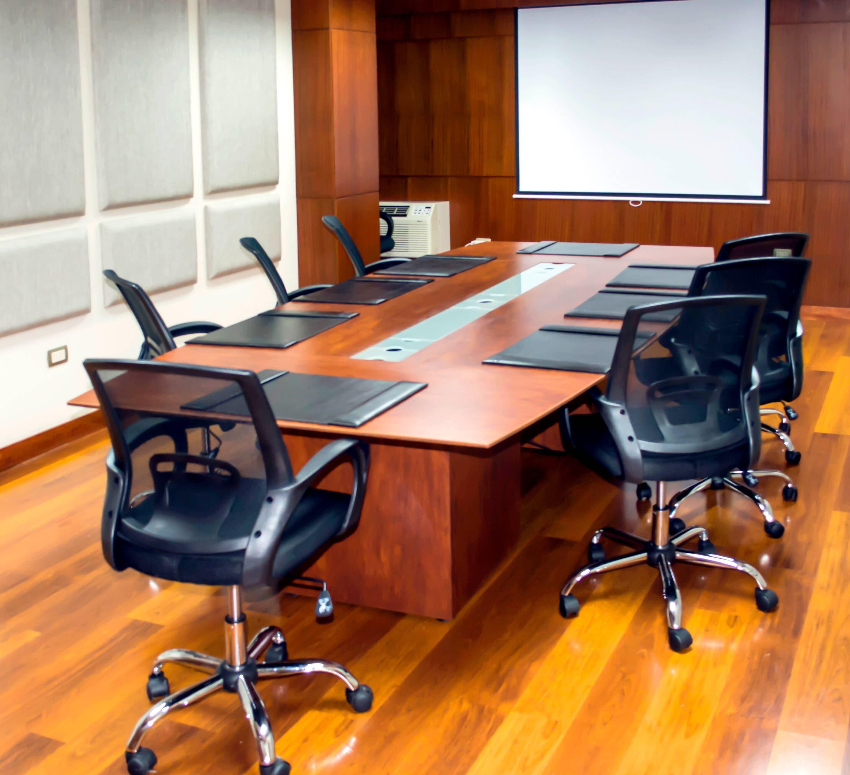 A conference room with a long wooden table, black office chairs, a projector screen, and a whiteboard.
