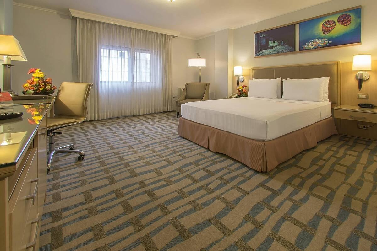 Een hotelkamer met een groot bed, een bureau met een lamp, een stoel en een bureaulamp.