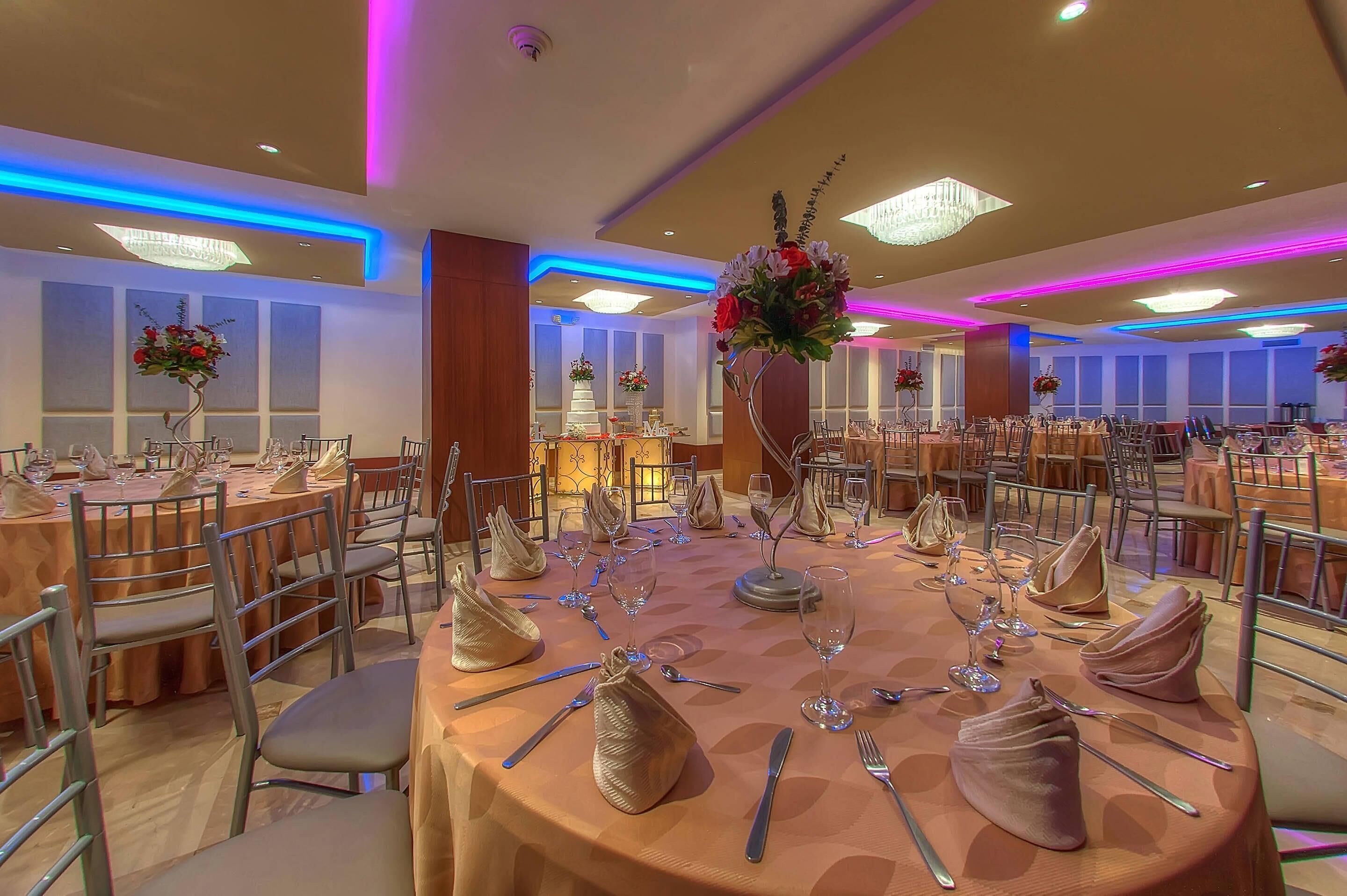 Un salón de banquetes con mesas redondas, sillas y centros de mesa florales.