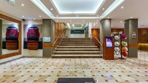 A hotel lobby with a check-in desk, a staircase, and a wall with a large screen.