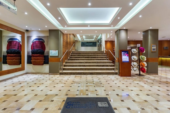A hotel lobby with a check-in desk, a staircase, and a wall with a large screen.