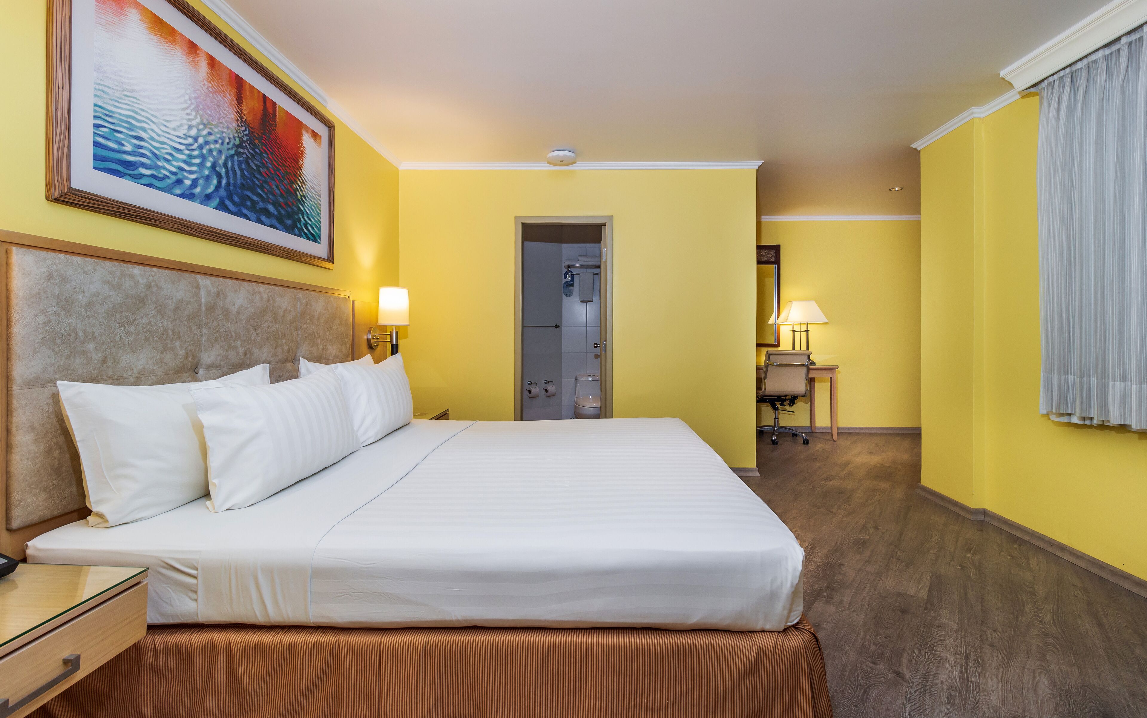 Een hotelkamer met een bed, nachtkastje, lamp en een schilderij aan de muur.