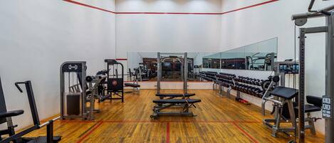 Un gimnasio con diversos equipos de ejercicio, un espejo grande y suelo de madera.