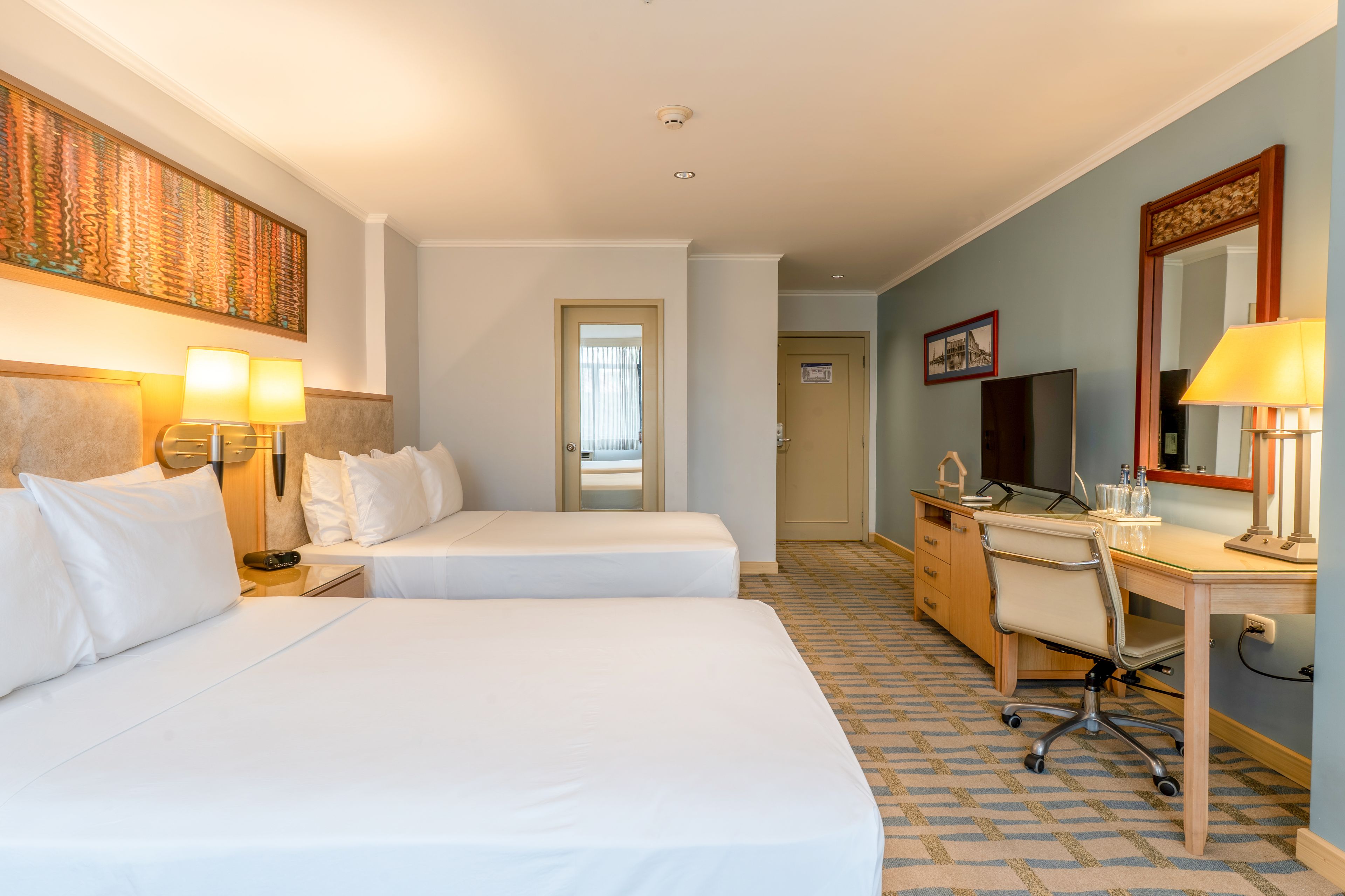 A hotel room with two beds, a desk, a chair, a television, and a bathroom door.