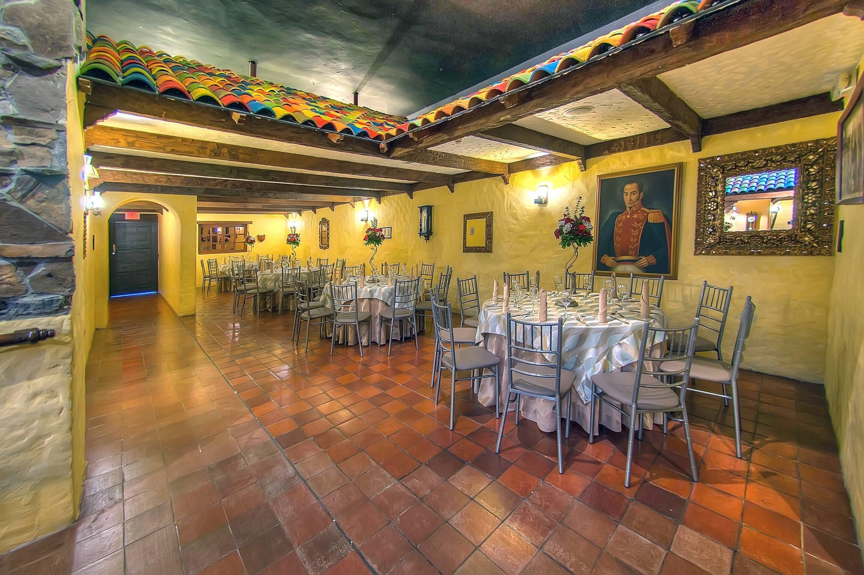 A dining area with multiple round tables set for guests, featuring a tiled floor and a high ceiling with exposed beams.