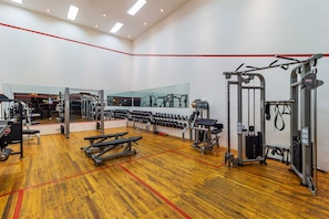 Een sportschool met trainingsapparatuur, banken en een spiegelwand.