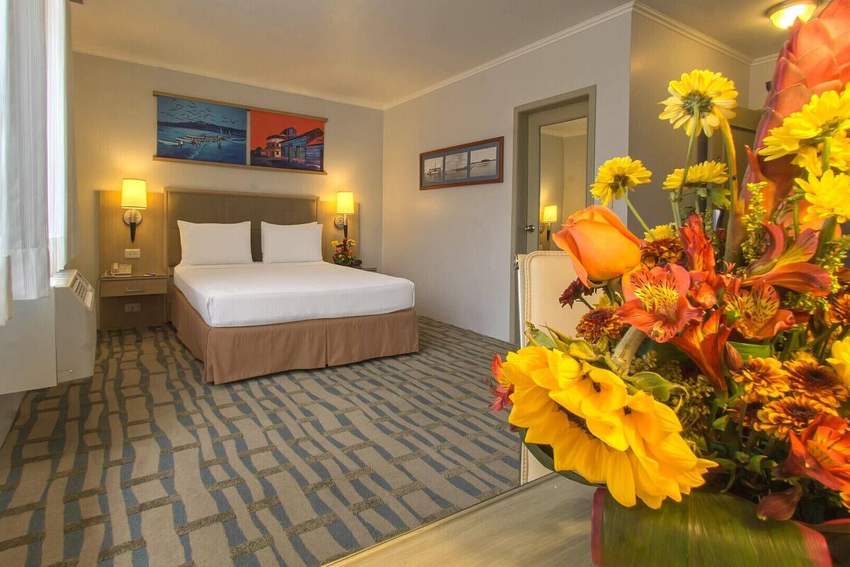Een hotelkamer met een bed, twee bedlampen, een grote spiegel, een bloemstuk en twee schilderijen aan de muur.