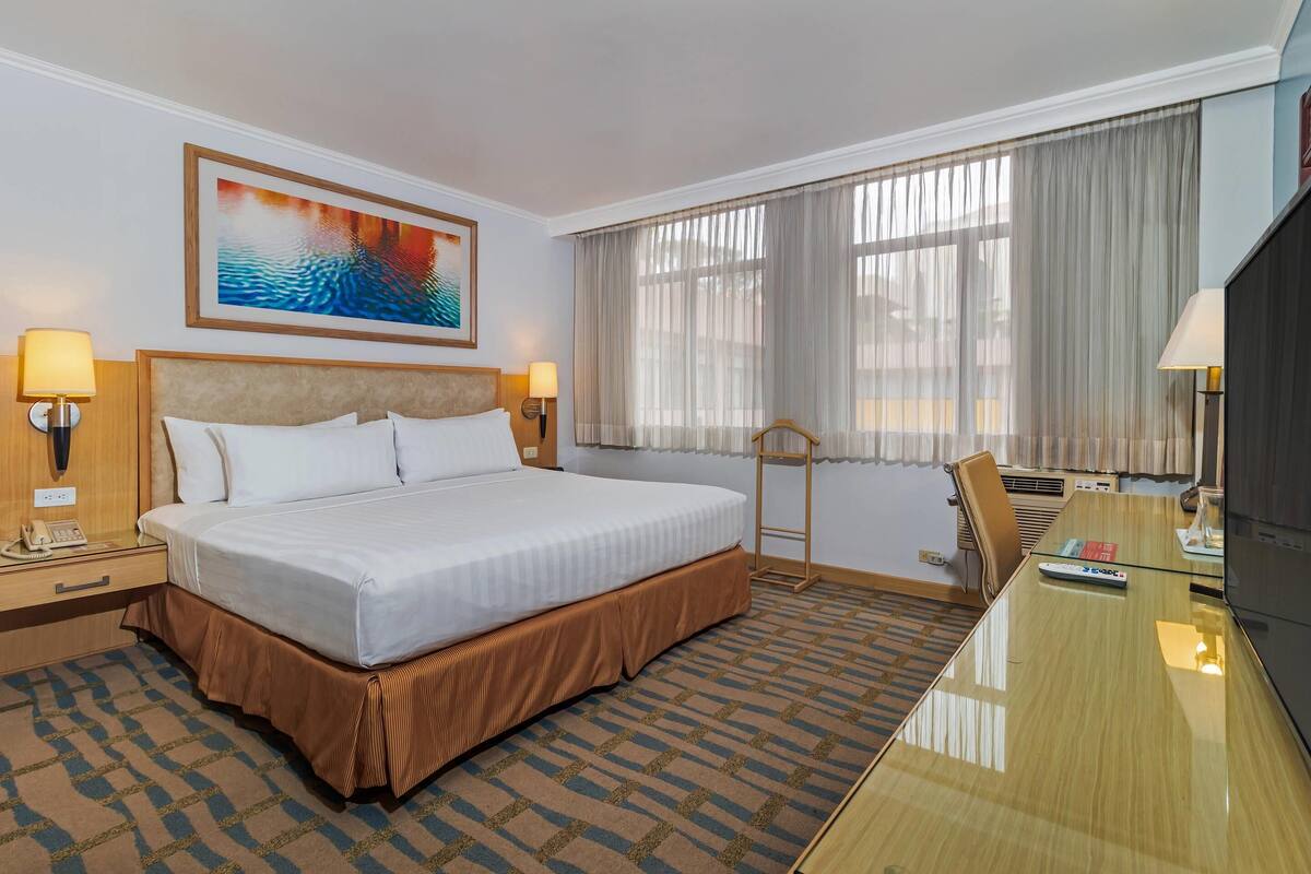 Een hotelkamer met een groot bed, bedlampen, een bureau en een televisie.