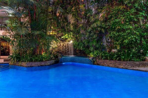 Una piscina interior con cascada, rodeada de exuberante vegetación tropical.