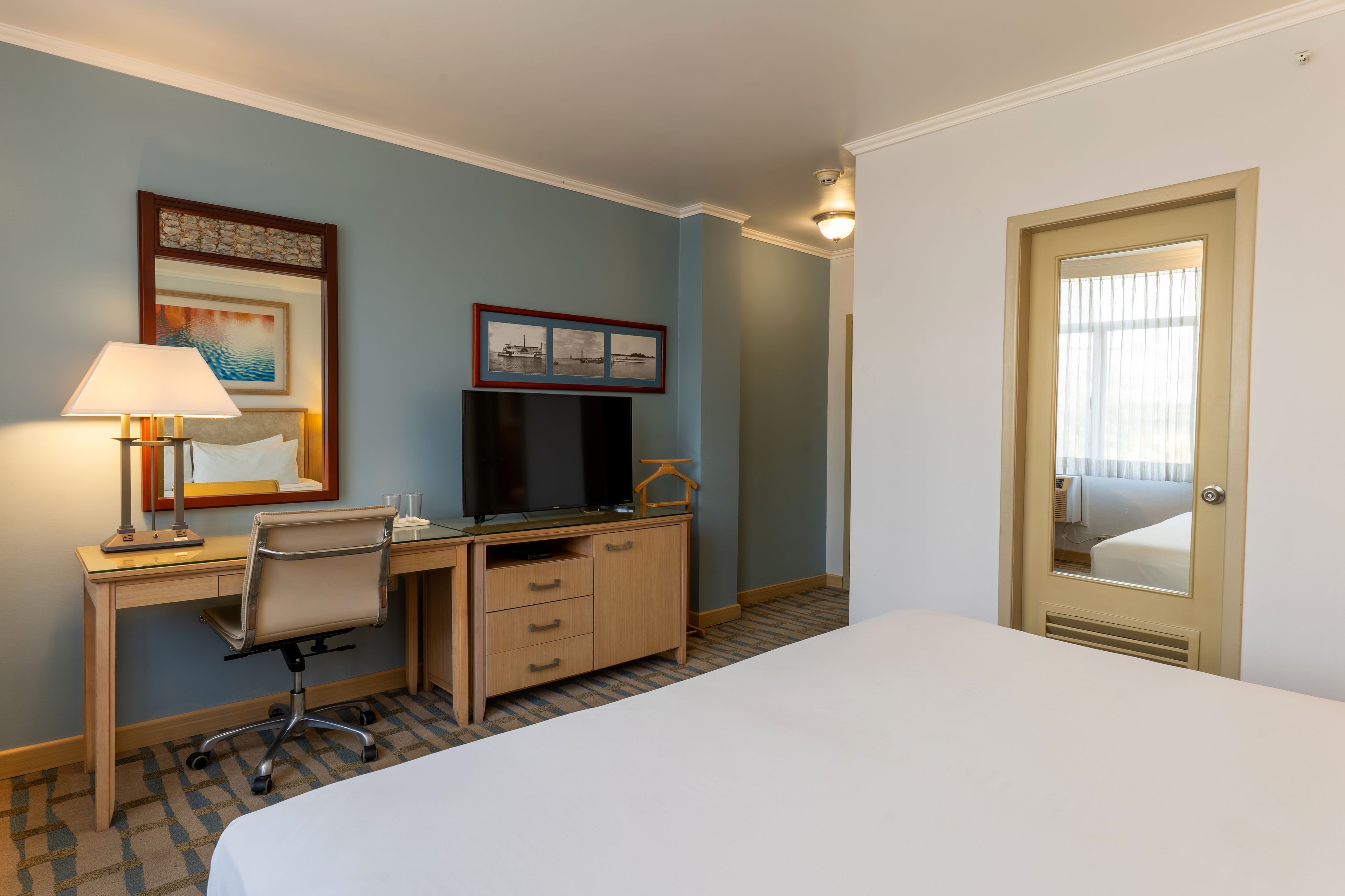 Habitación de hotel con cama, escritorio, silla, televisor y un cuadro en la pared.