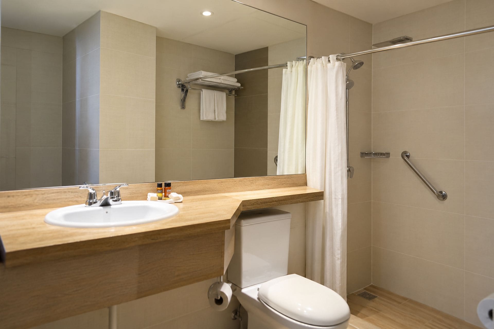 Un baño moderno con tocador de madera, un lavamanos blanco, un inodoro y una ducha con puerta de vidrio.