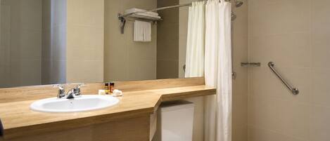 Un baño moderno con tocador de madera, un lavamanos blanco, un inodoro y una ducha con puerta de vidrio.