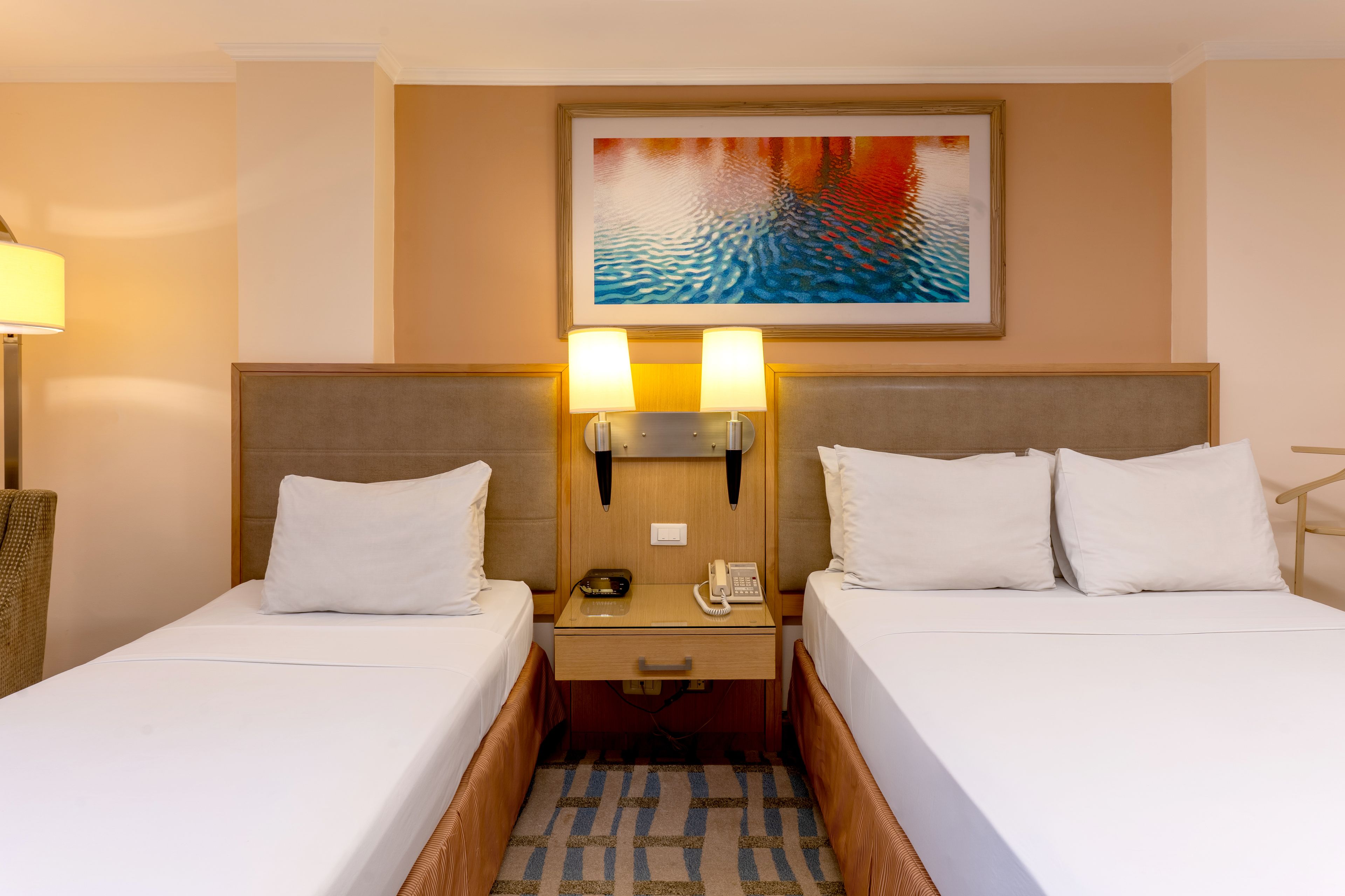 Une chambre d’hôtel avec deux lits, une table de chevet avec un téléphone et un tableau au-dessus de la tête de lit.
