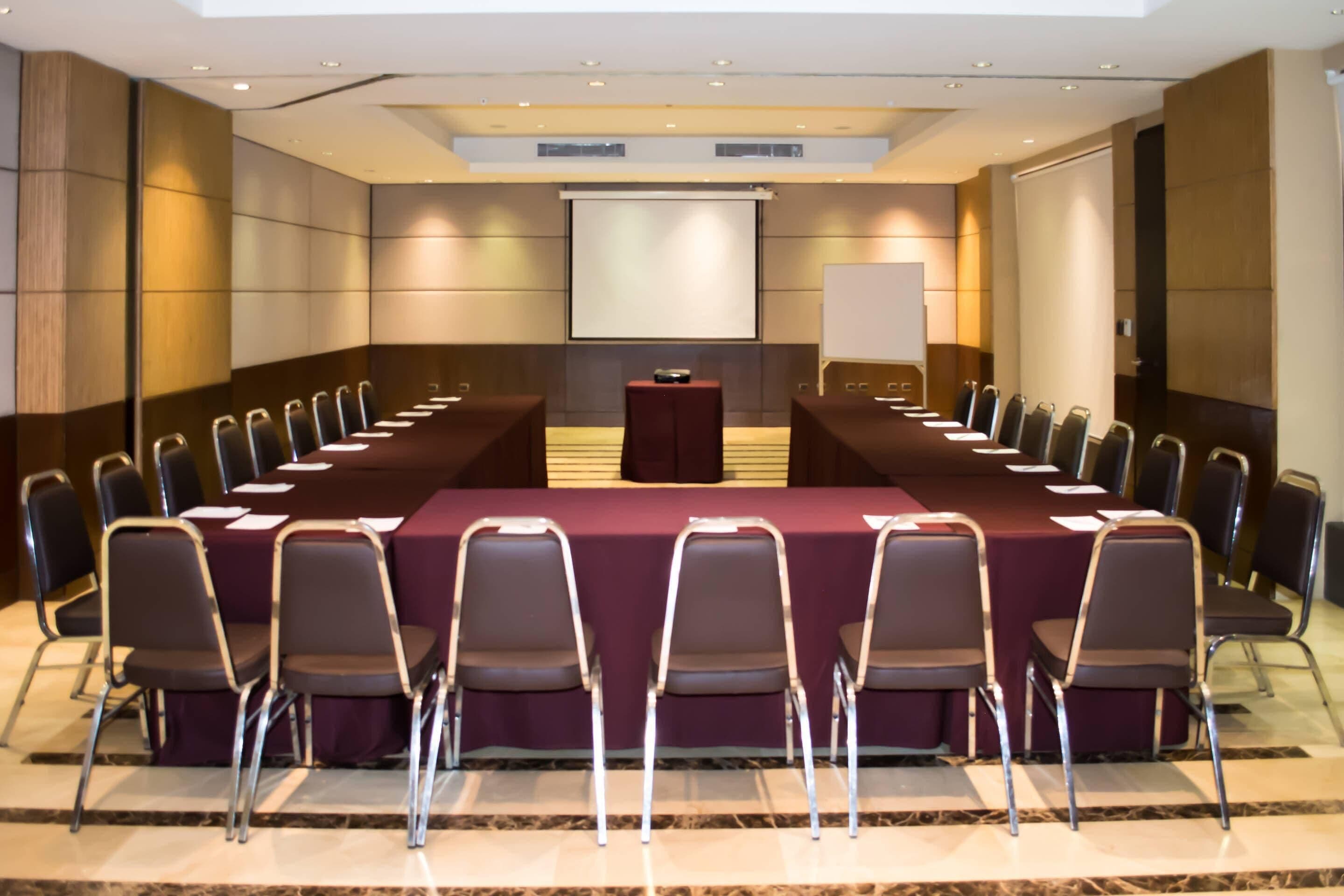 Une salle de conférence équipée d’une longue table, de chaises, d’un pupitre et d’un écran de projection.