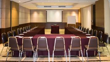 Une salle de conférence équipée d’une longue table, de chaises, d’un pupitre et d’un écran de projection.