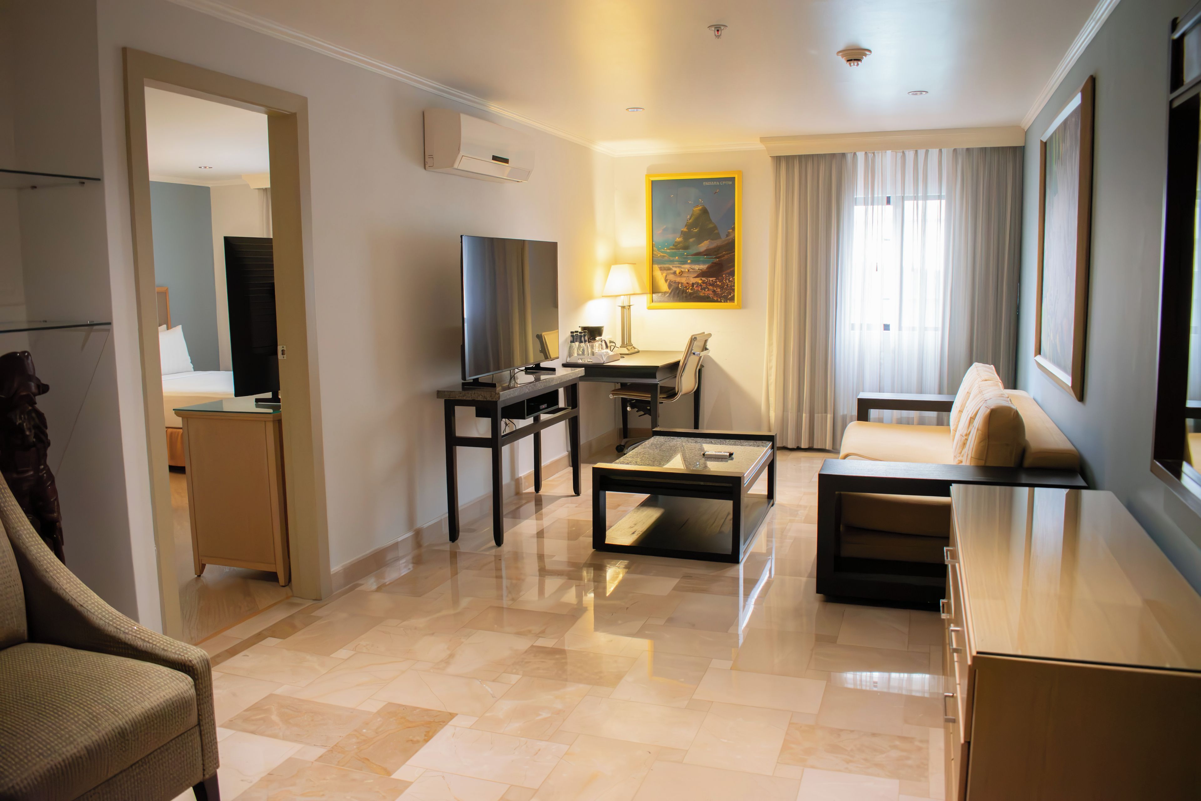 A hotel room with a seating area, a desk, a television, and a painting on the wall.