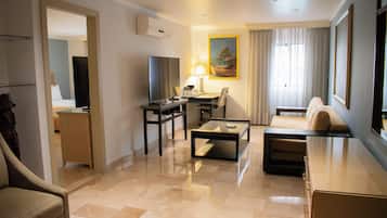 A hotel room with a seating area, a desk, a television, and a painting on the wall.