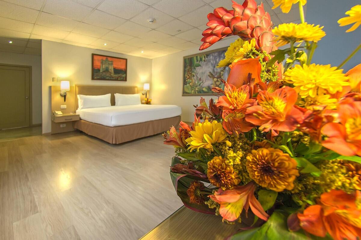 Een hotelkamer met een bed, nachtkastjes, een schilderij aan de muur en een bloemstuk op de tafel.
