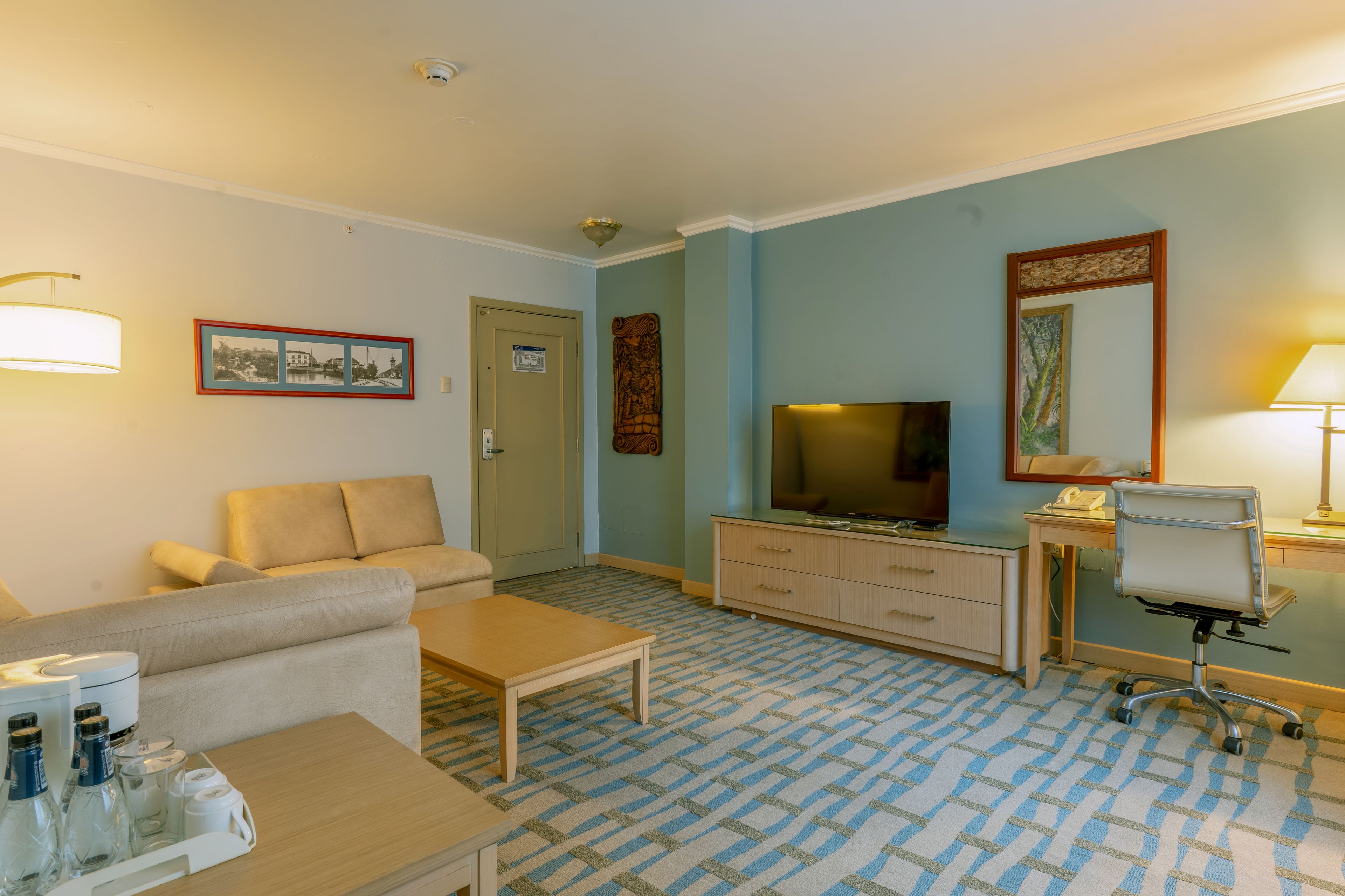 Habitació d'hotel amb sofà, televisió, escriptori amb cadira, taula de centre i una catifa estampada.