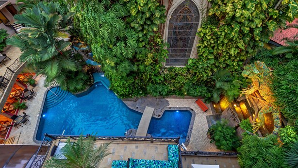 An aerial view of a hotel with a swimming pool surrounded by lush greenery and a decorative garden.