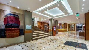 A spacious lobby with a tiled floor, a staircase, and a reception desk.