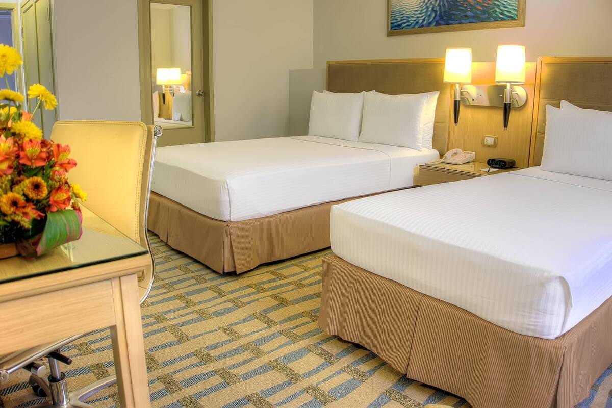 Een hotelkamer met twee eenpersoonsbedden, een nachtkastje met lamp, telefoon en een bloevas.