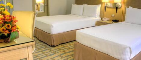 A hotel room with two single beds, a bedside table with a lamp, a telephone, and a vase of flowers.