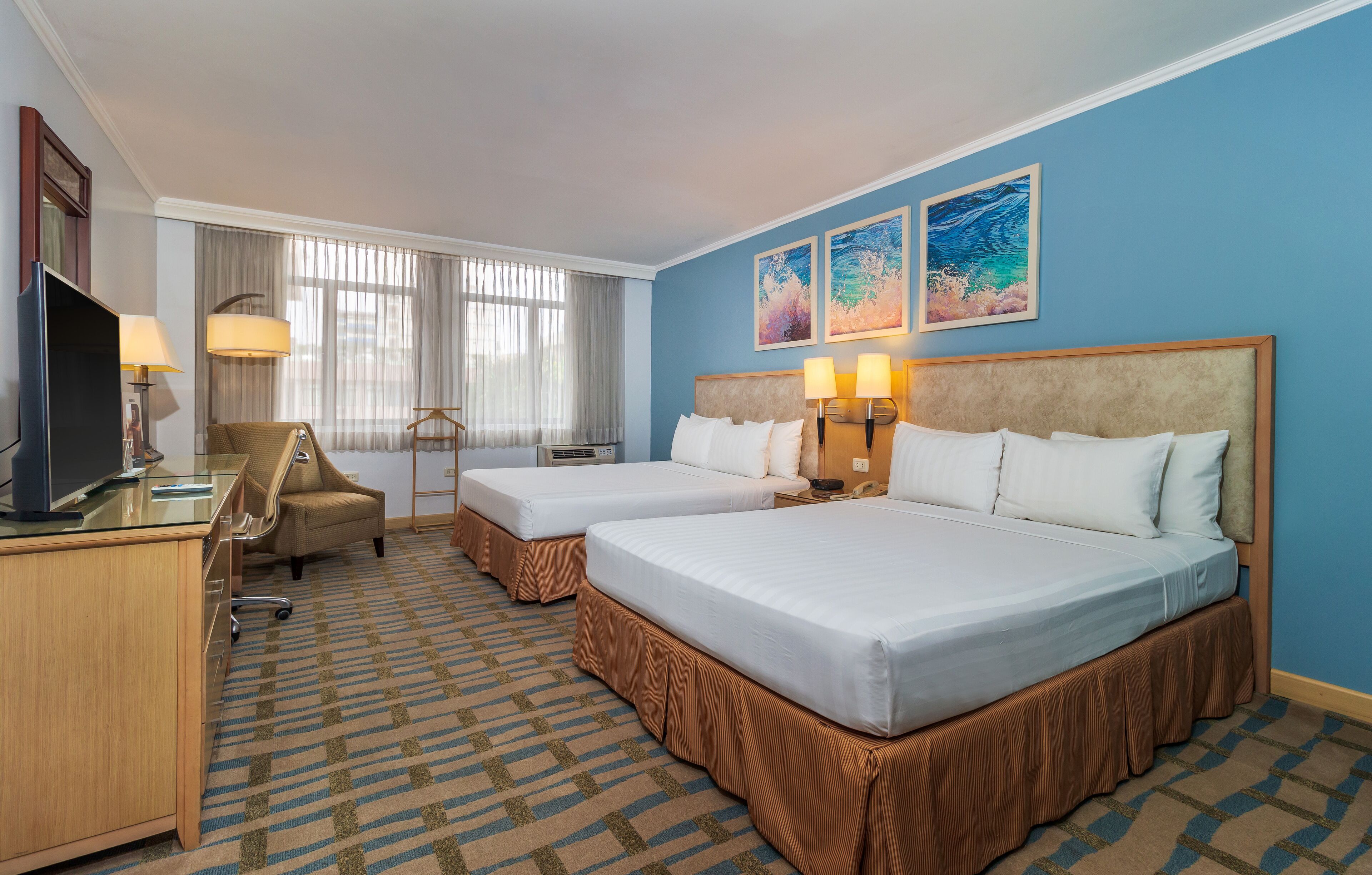 A hotel room with two beds, a desk, a chair, and a TV.