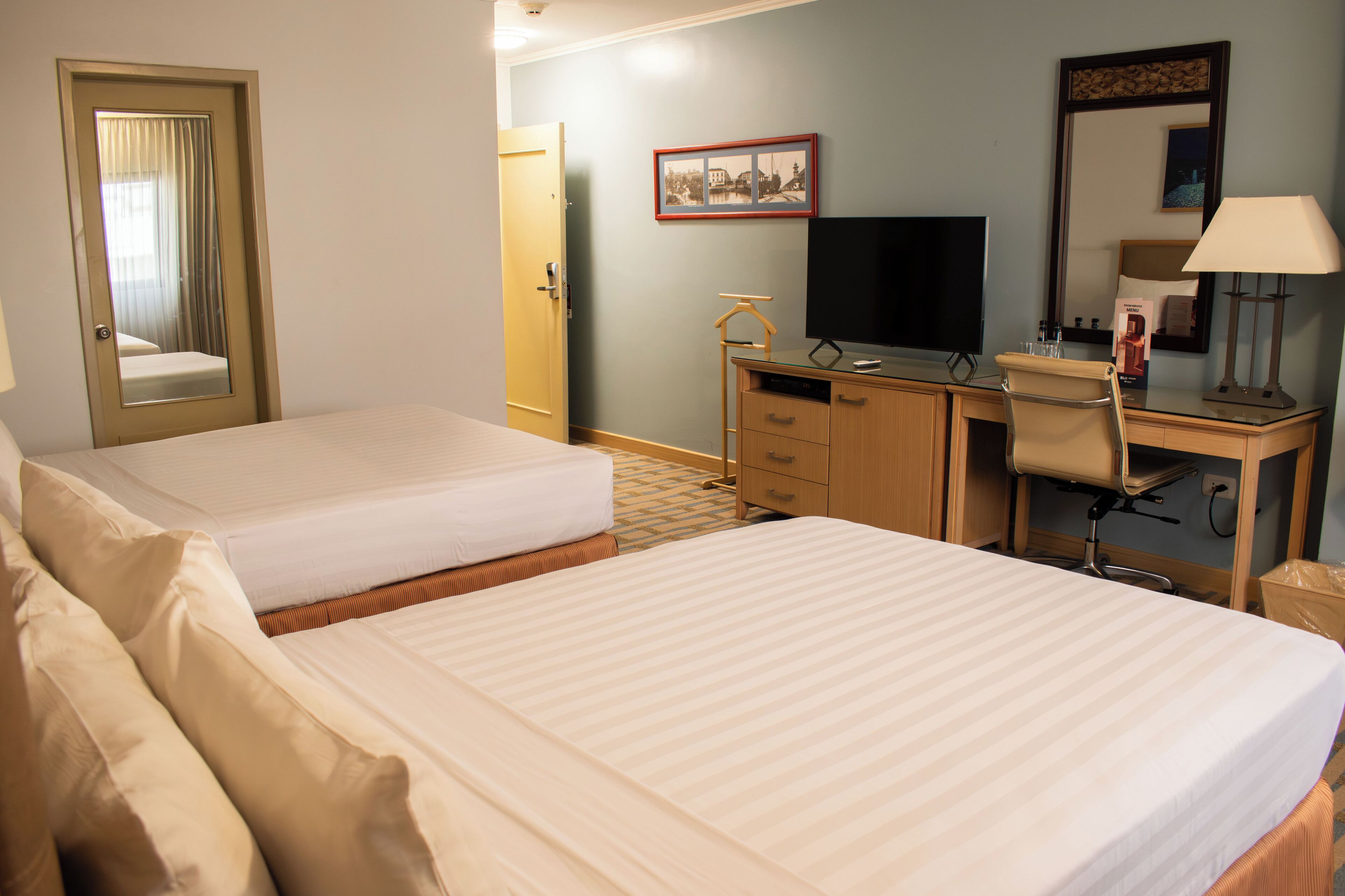 A hotel room with two beds, a desk with a computer, a chair, a television, and a mirror.