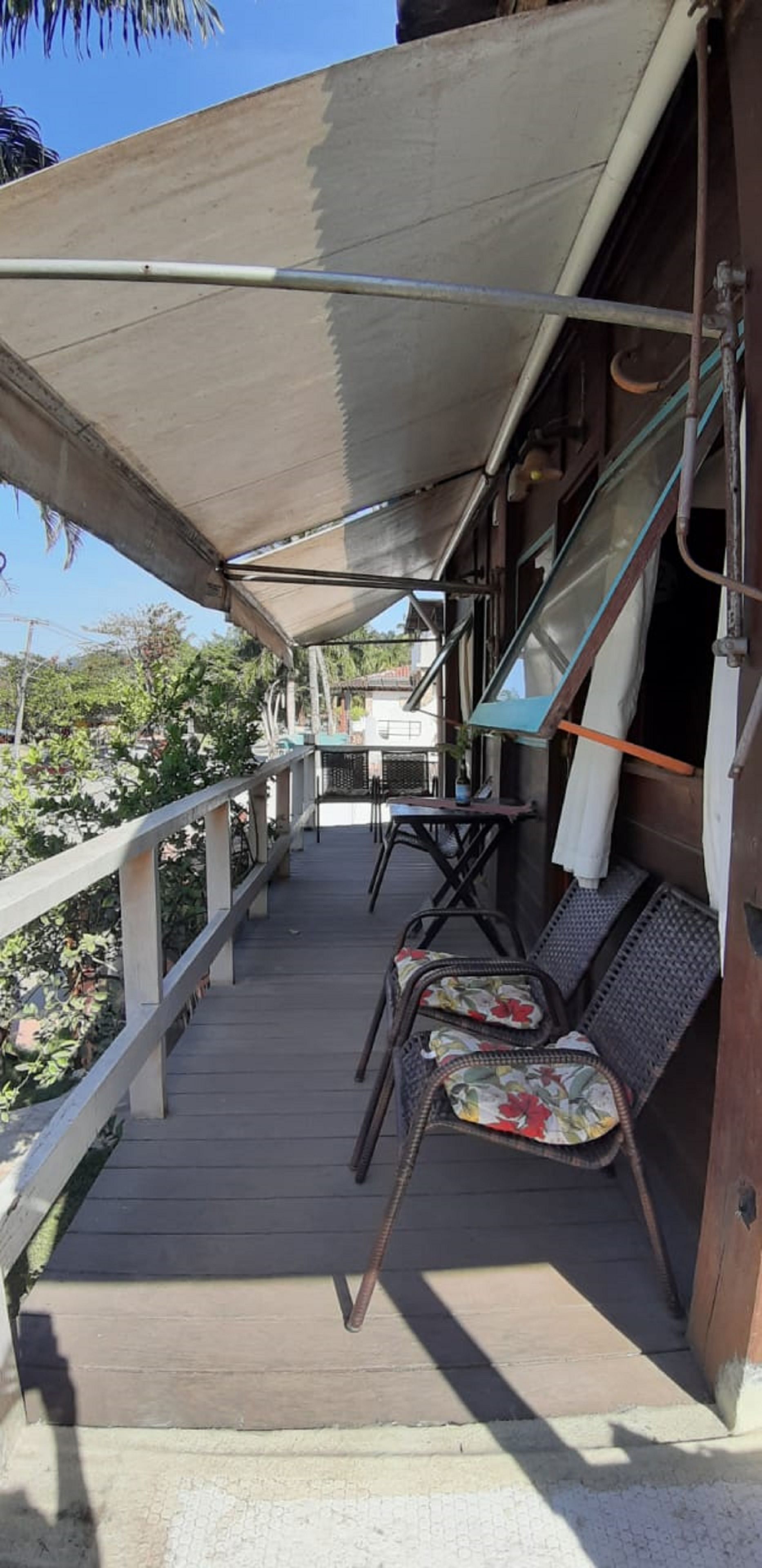 A covered outdoor area with a wooden deck, metal railings, and wicker chairs with floral cushions.